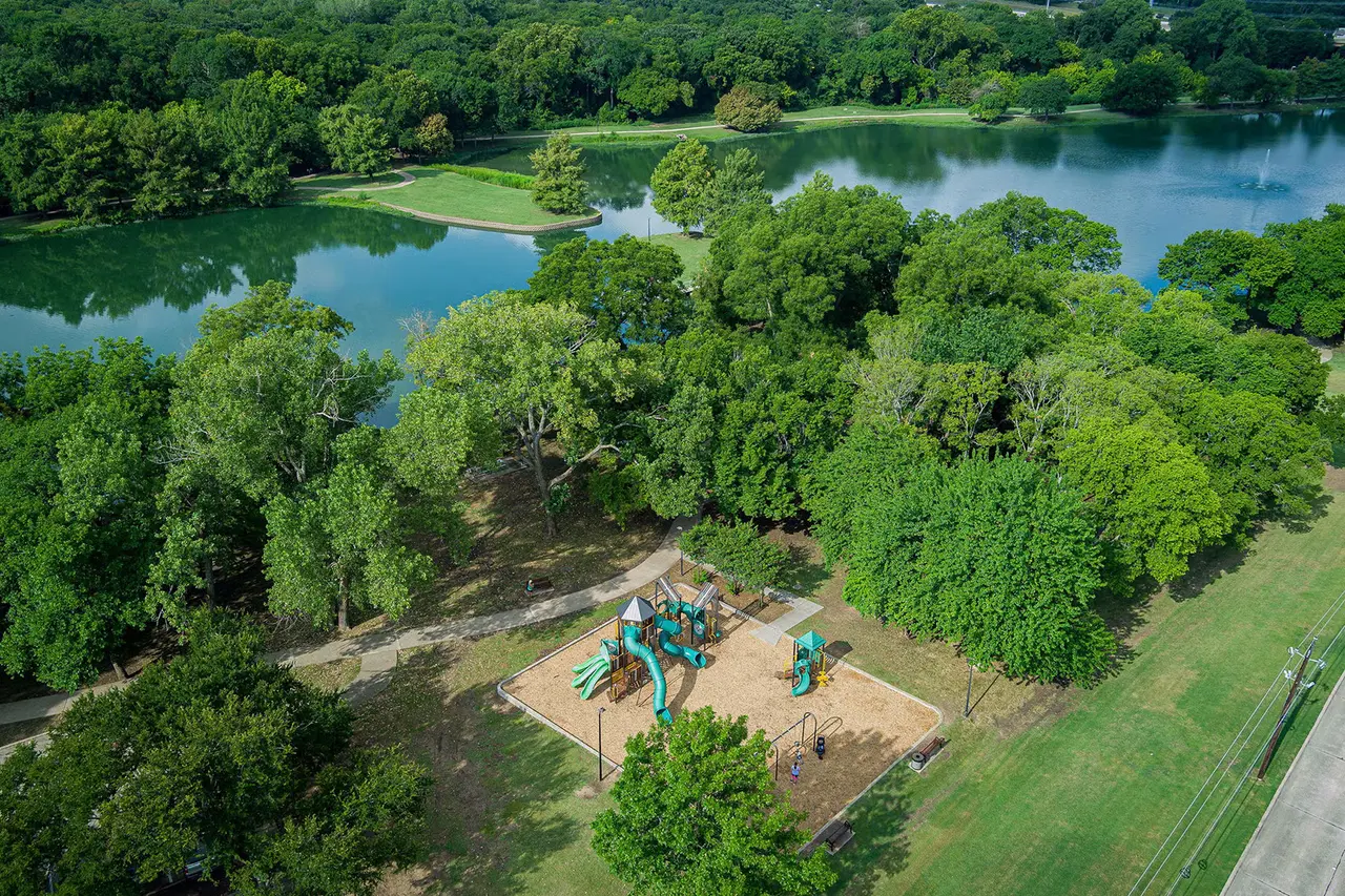 Aerial view of playground with turquoise equipment beside forested park and blue lake waters