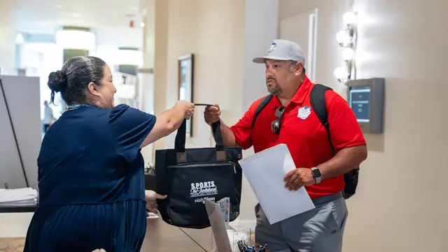 Man taking a bag from a woman behind a table after checking into an event
