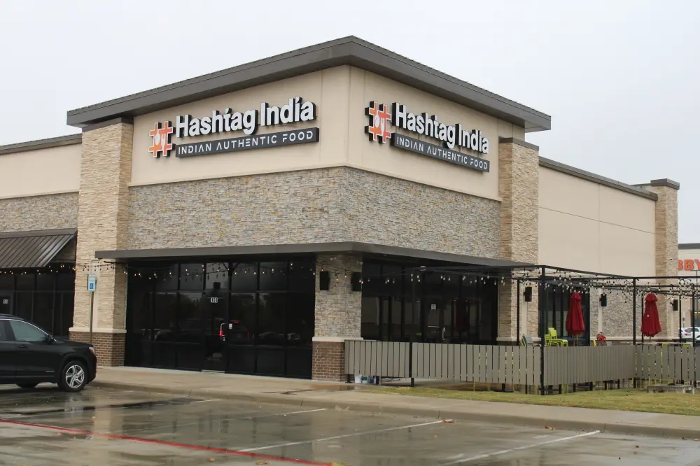 Brick storefront with large signage and dark windows in a shopping center parking lot