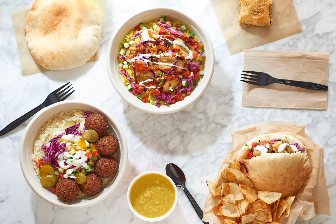 Overhead view of Mediterranean bowls and wraps with hummus, falafel, fresh vegetables, pita bread, and crispy chips on marble surface