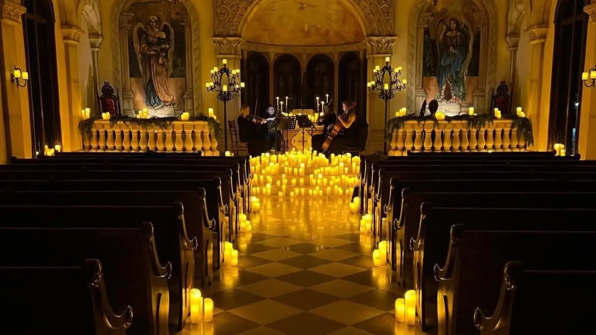 Historic chapel with wood pews lined with candles down the aisle that lead to a symphony