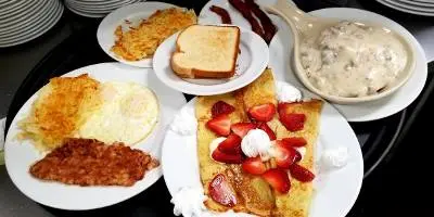 Breakfast spread with eggs, bacon, toast, waffles with fruit, hash browns, and side of potatoes on white plates