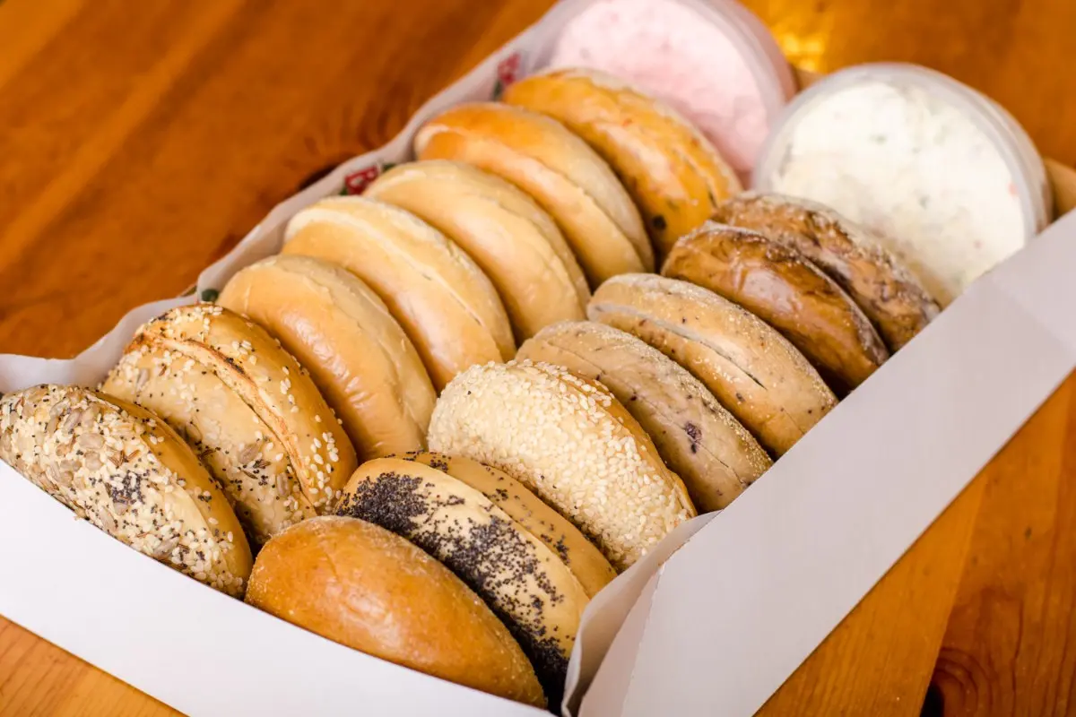 Assorted bagels in a white box, including plain, seeded, cinnamon raisin, and flavored varieties with cream cheese spreads
