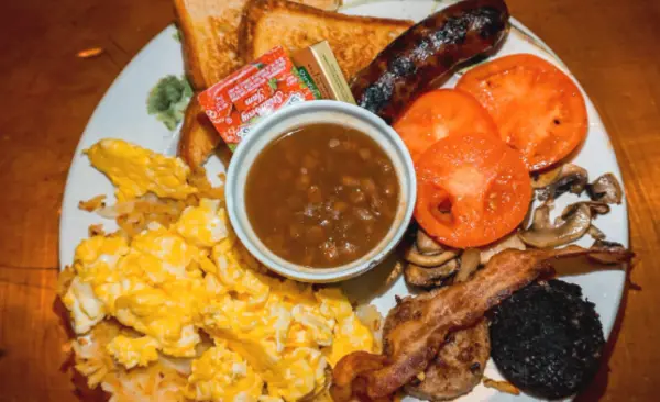bangers and mash, scrambled eggs, roasted tomatoes, and toast on a white dining plate