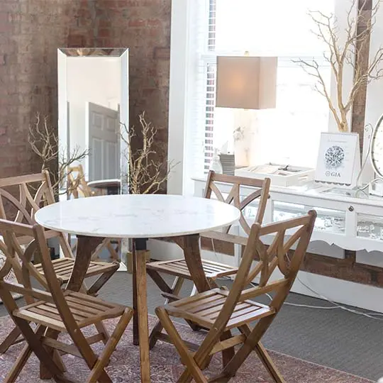 Round marble table with wooden chairs in bright showroom with brick walls and desk display area