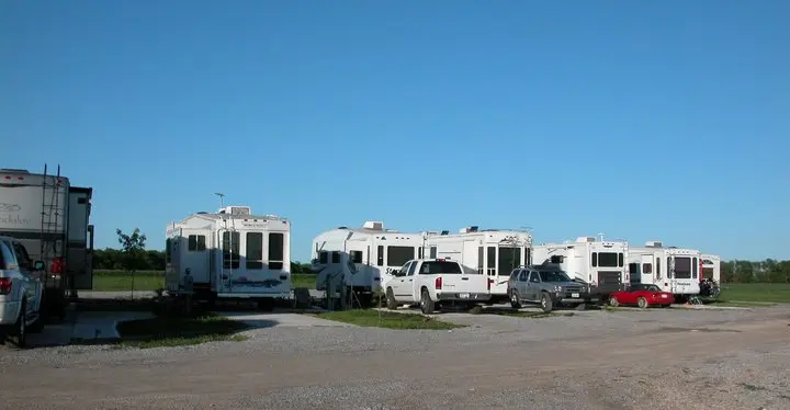 Row of white and colored RV trailers parked in gravel lot under clear blue sky