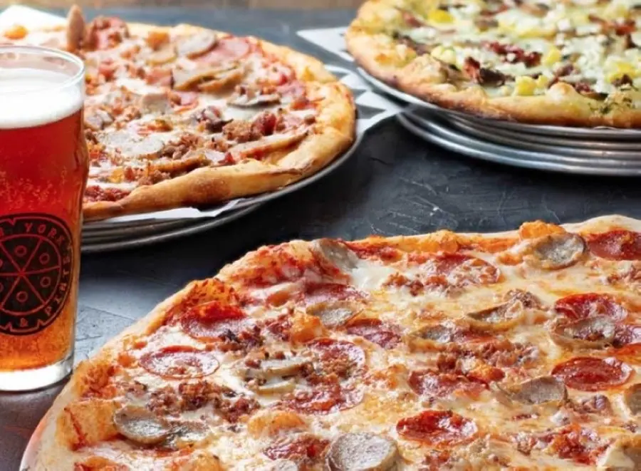 Multiple pizzas with various toppings and a glass of beer on dark surface