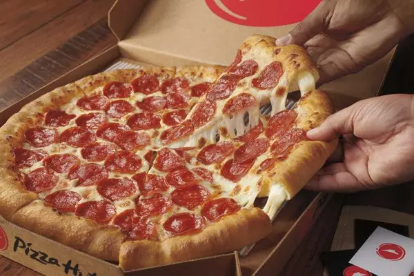 Hands holding a slice of pepperoni pizza with melted cheese stretching from the pie on a cardboard box