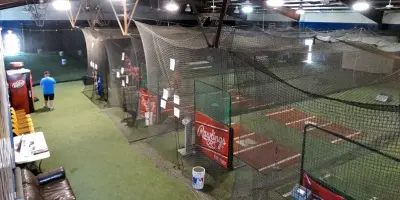 Indoor baseball and softball facility with multiple batting cages, green turf, and netting