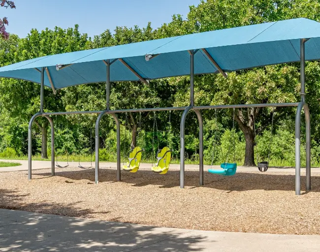 Blue canopy shelter over playground with swings and trees in background