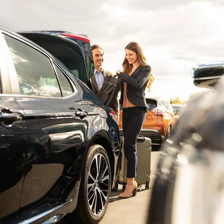 Man and woman examining black SUV with open door at car rental lot