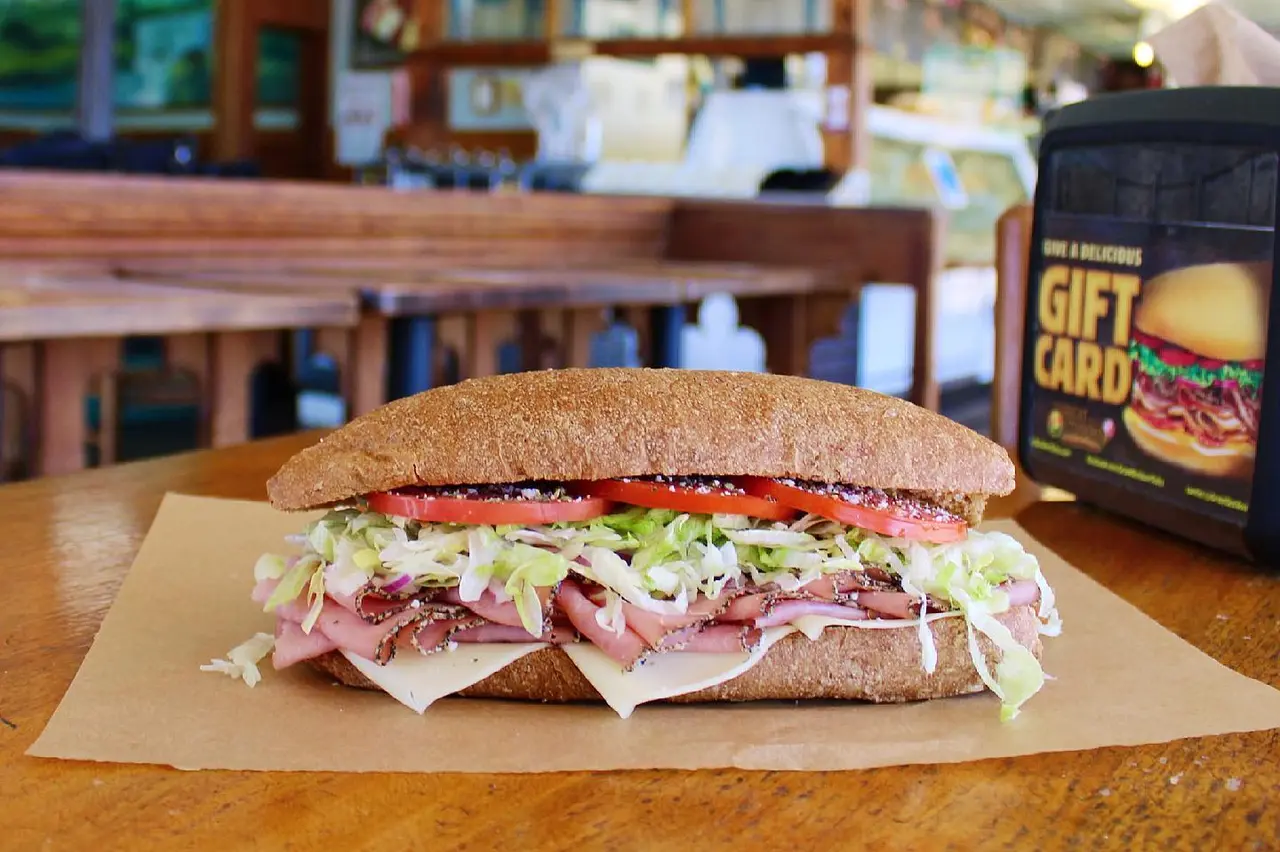 Sliced ham and cheese sub sandwich with lettuce and tomato on whole wheat bread, served on paper on wooden table
