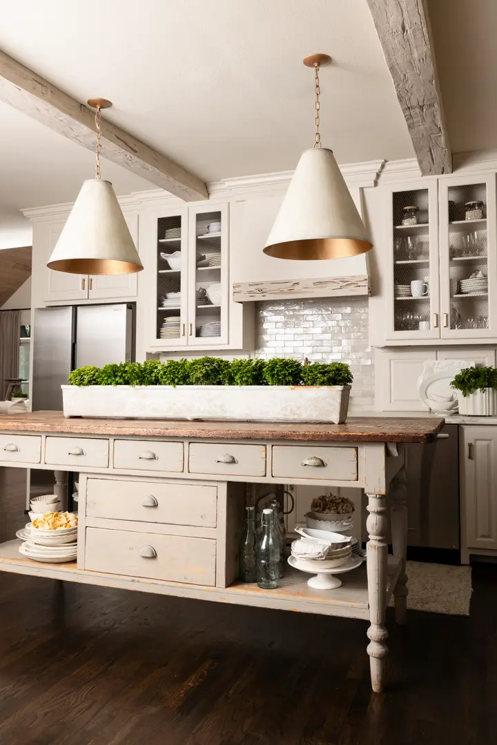 Modern farmhouse kitchen with cream cabinetry, white subway tile backsplash, wooden island with pendant lights, and potted greenery centerpiece