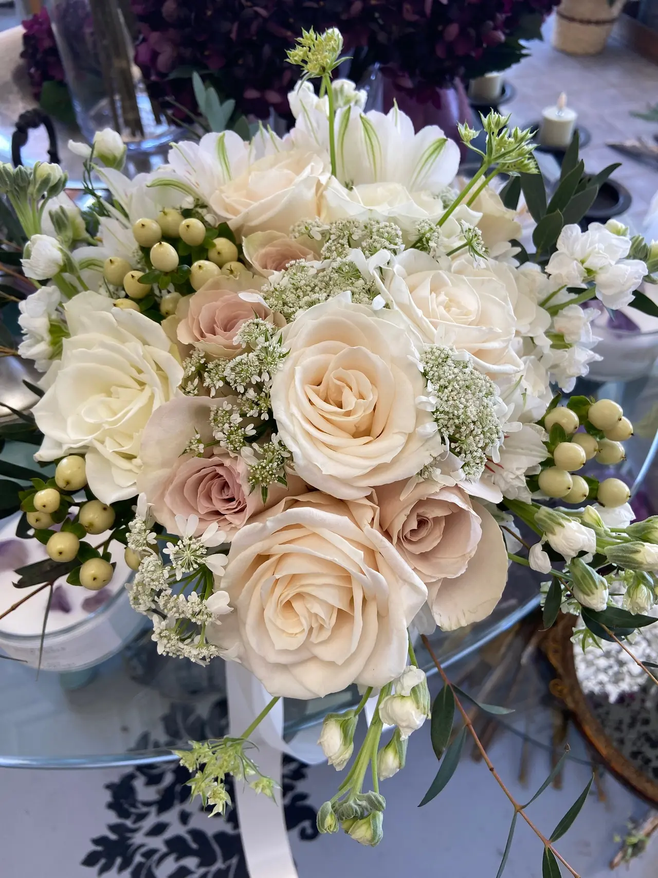 Bridal bouquet of cream and blush roses, white ranunculus, baby's breath, and green hypericum berries with trailing greenery