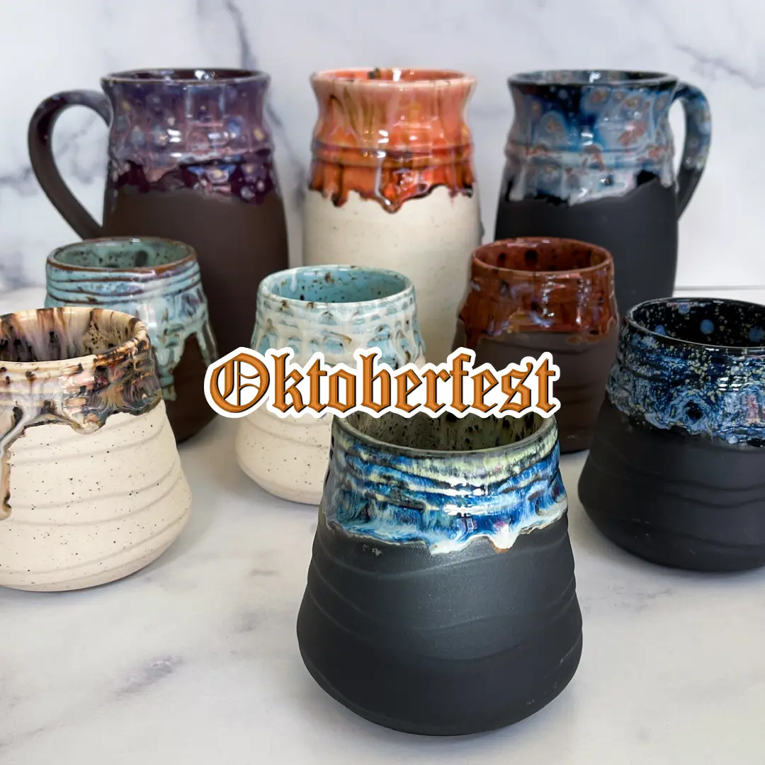 Hand-thrown ceramic mugs and steins with glazed rims in earthy tones displayed on marble surface