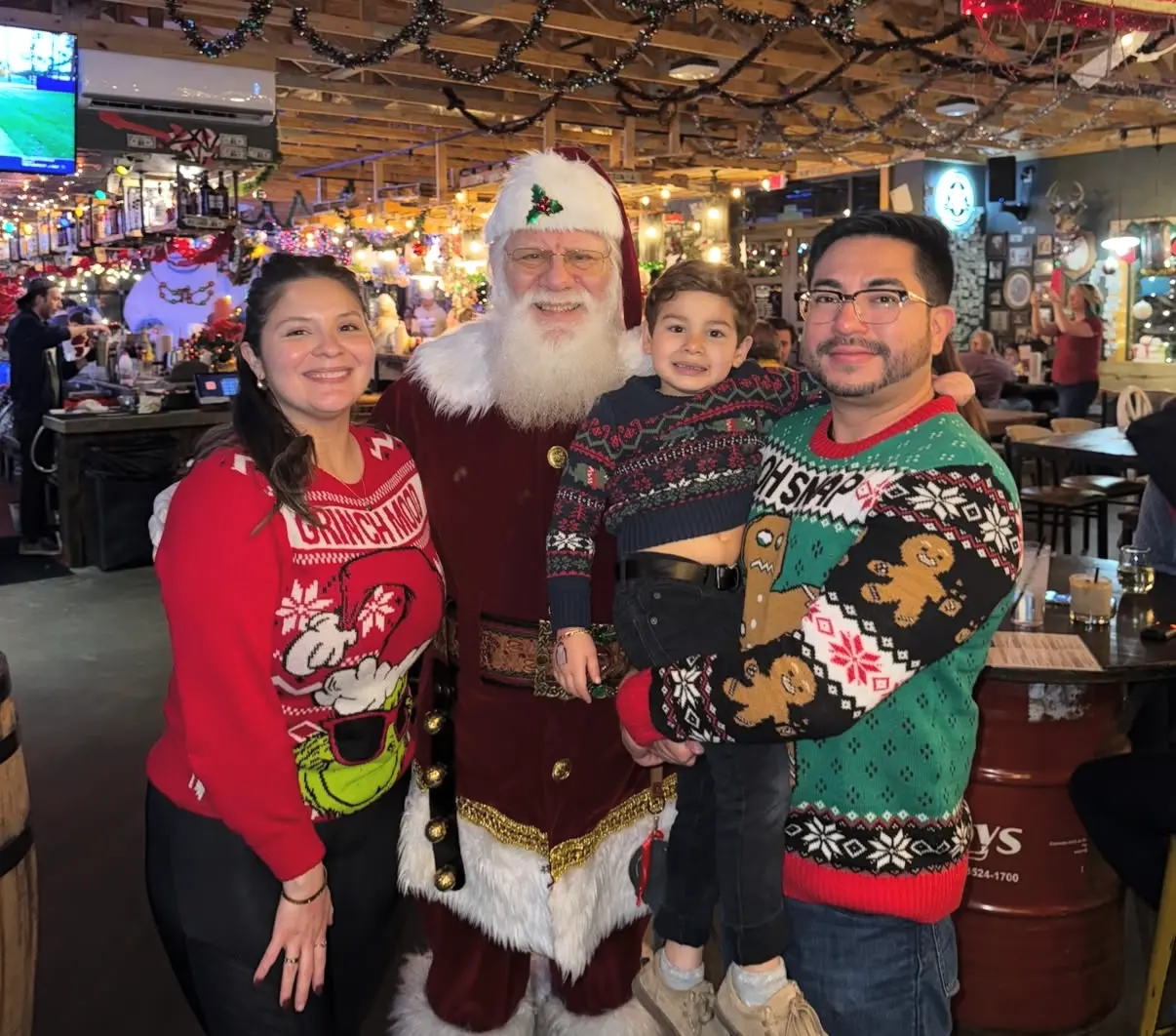 Family in ugly Christmas sweaters posing with Santa Clause in a restaurant