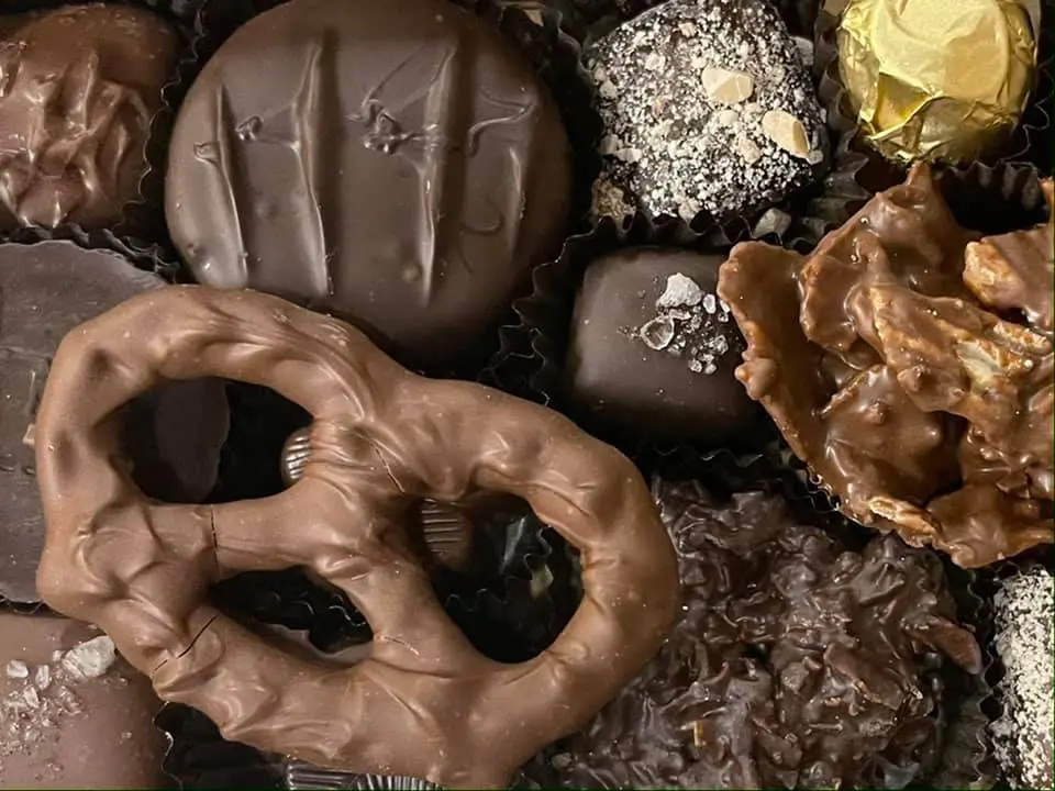 Assorted chocolate candies including dark chocolate truffles, pretzel-shaped milk chocolate, and coconut-topped pieces arranged closely together