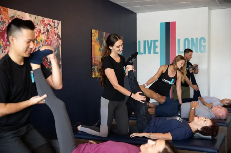 Group of instructors performing assisted stretching with clients lying on mats in a fitness studio