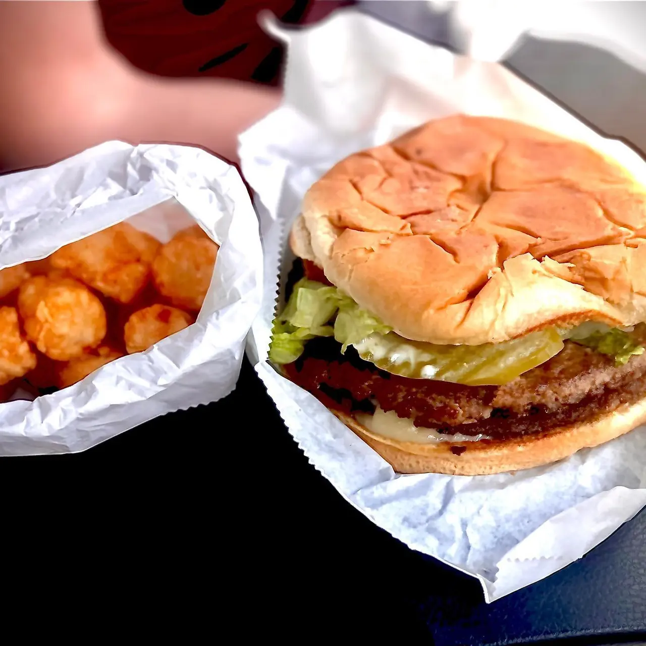 Burger with lettuce and meat patty alongside fried cheese curds in paper wrapper