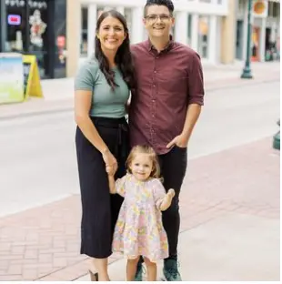 A man and woman with a young child standing together on a downtown street lined with storefronts