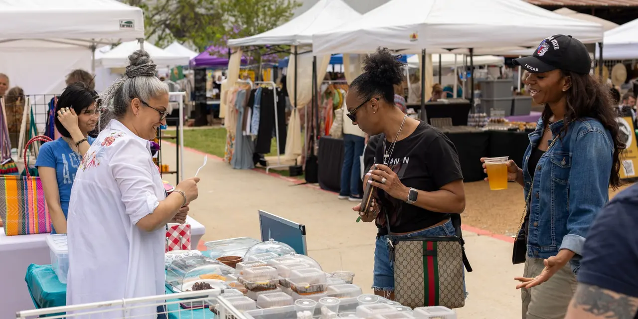 Outdoor market vendor tents with shoppers browsing clothing and handmade goods at a brewery event under white canopy tents