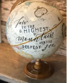 Painted globe with handwritten text reading "love to the highest mountain and the deepest sea" on wooden stand