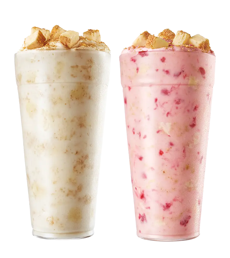Two tall glasses of blended ice drinks topped with crushed candy pieces, one cream-colored and one pink