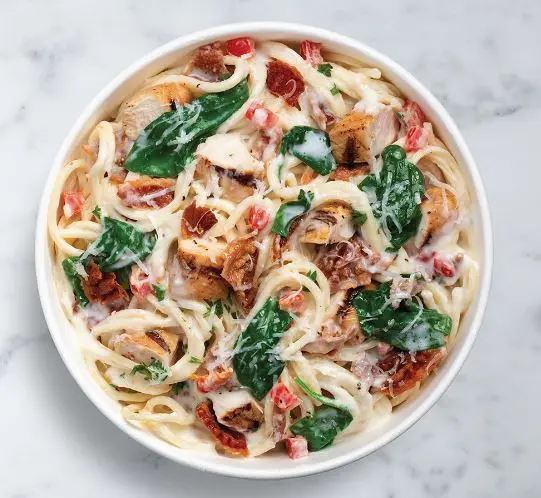 Creamy pasta dish with bacon, spinach, and red peppers in a white bowl