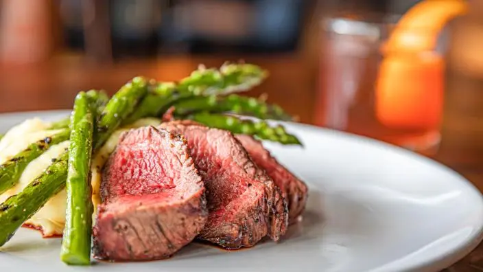 Medium-rare sliced beef steak with roasted asparagus on a white plate