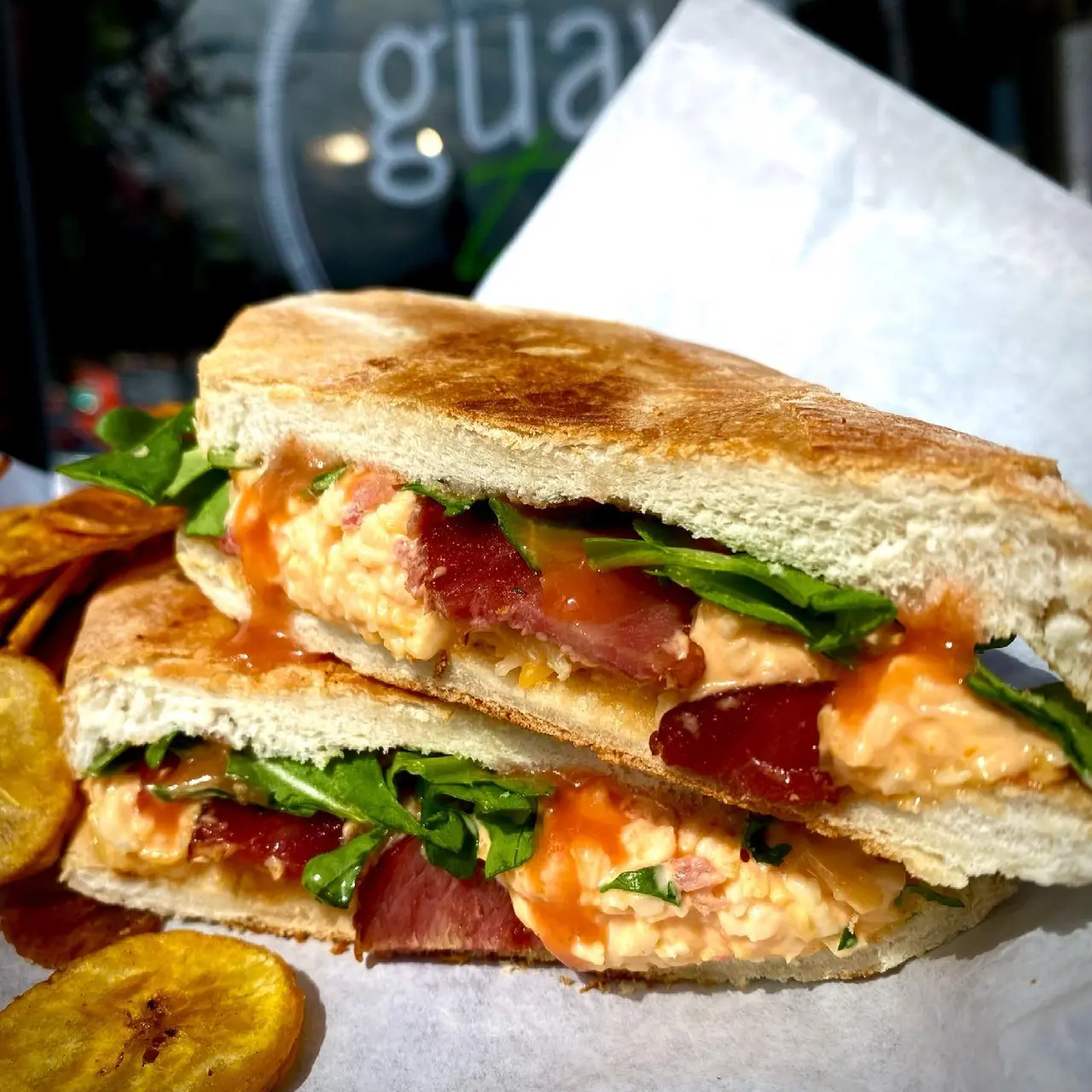 Stacked Cuban sandwich with cured ham, cheese, and greens on toasted bread, served with fried plantain chips