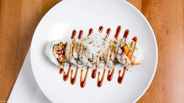 Sushi rolls topped with white cream and garnished with red sauce drizzle on a white plate