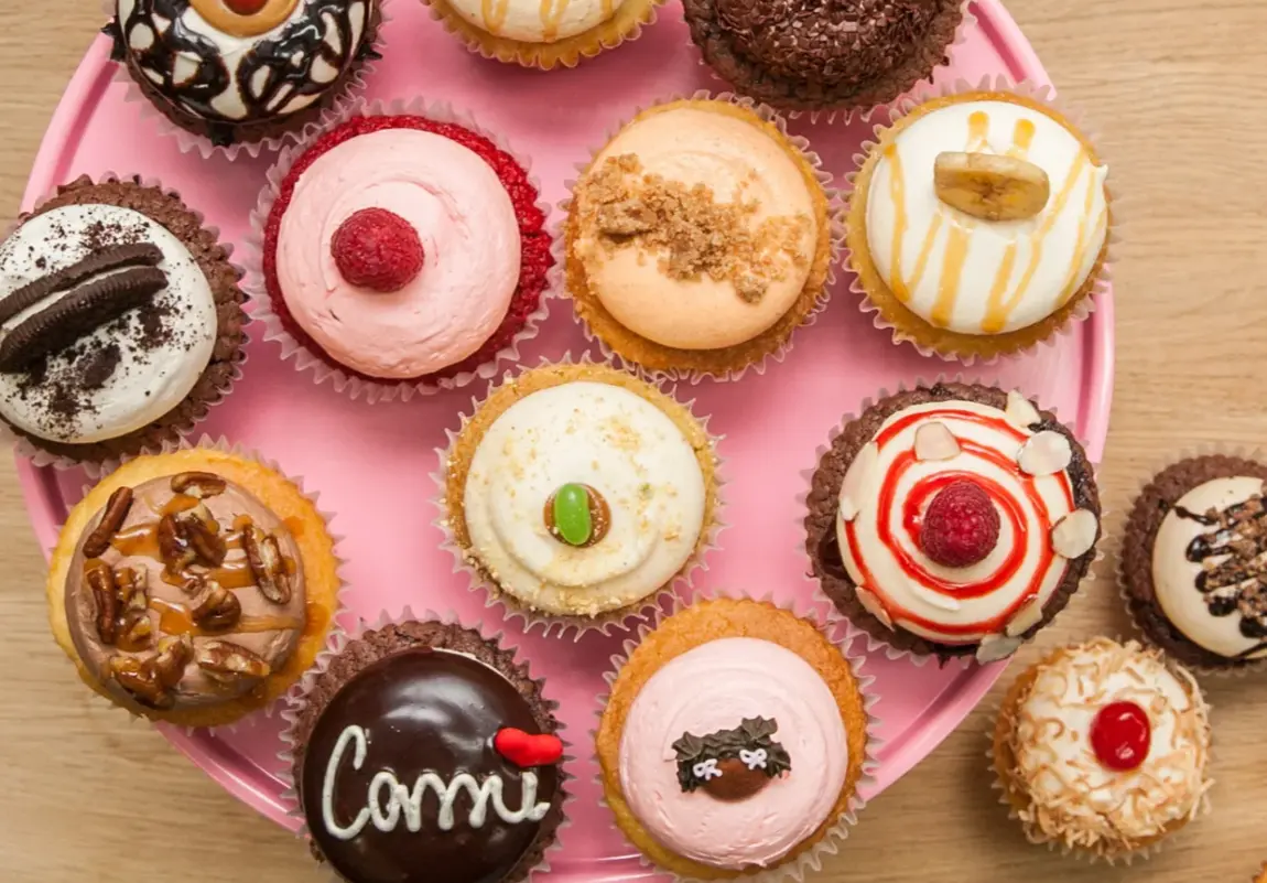 Assorted decorated cupcakes arranged on a pink circular plate on a wooden surface