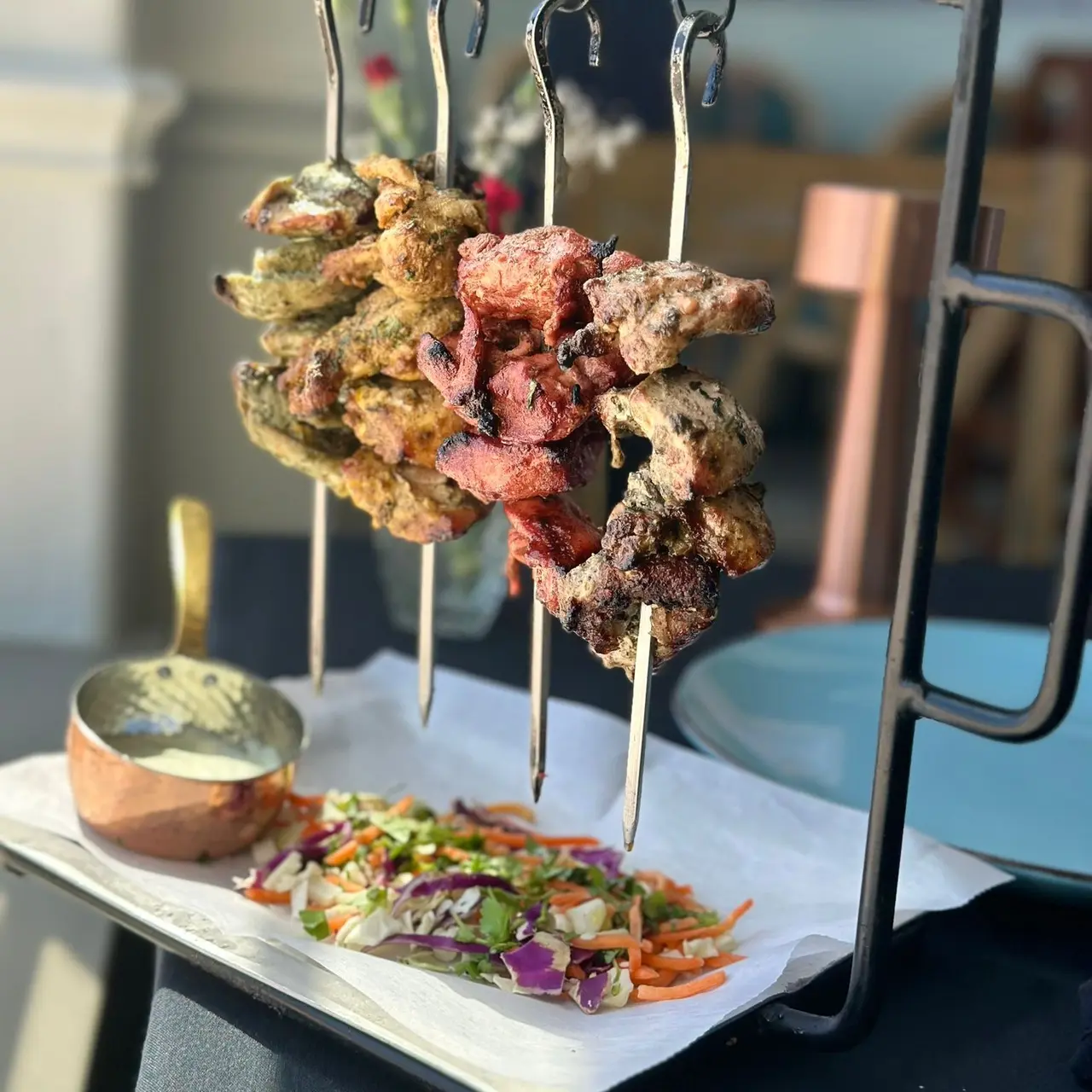 Grilled meat skewers with colorful spices served on white plate with fresh vegetable salad and sauce