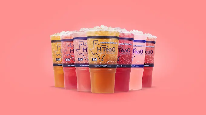 Six colorful bubble tea drinks with cream foam tops arranged in a circle against a pink background