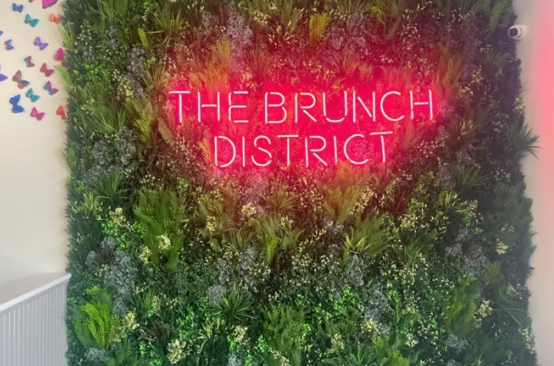 Neon sign glowing pink against a living plant wall of green moss and white flowers