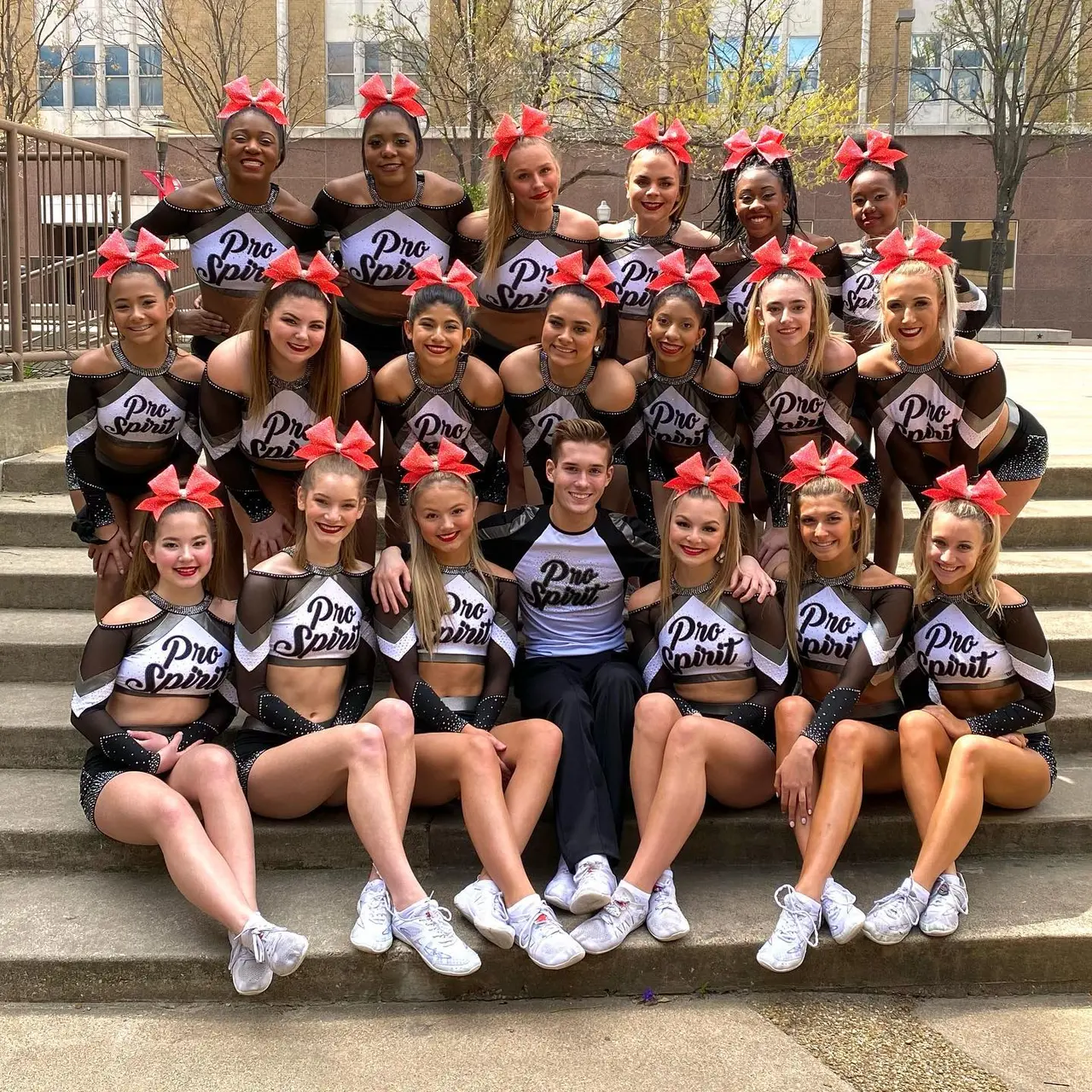 Cheerleading team in black and white uniforms with pink bows posed outdoors on steps