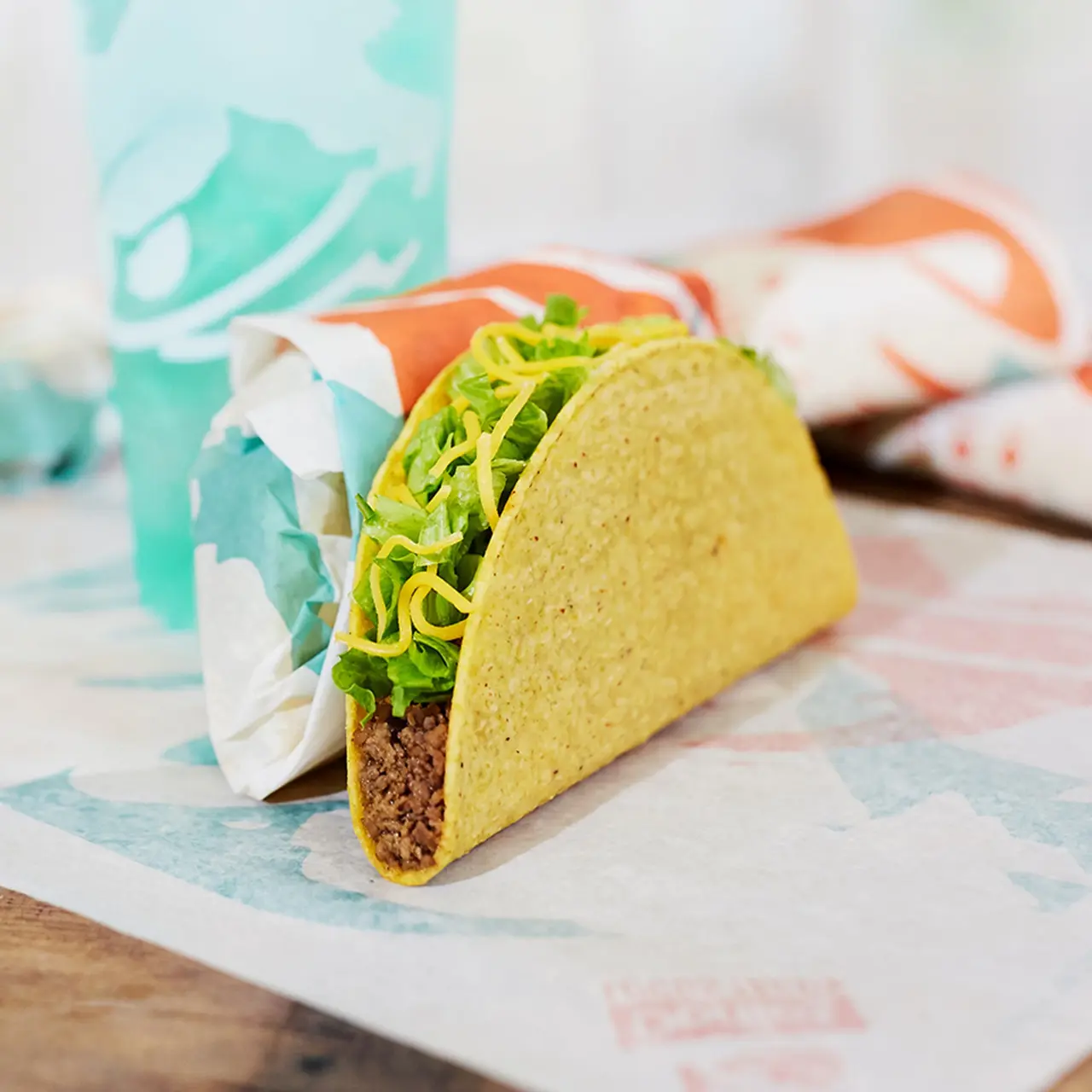 Crunchy yellow taco shell filled with seasoned meat, shredded lettuce, and white cheese in paper wrapper on branded napkin