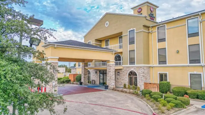 Yellow and stone hotel exterior with covered entrance, landscaped grounds, and clear blue sky