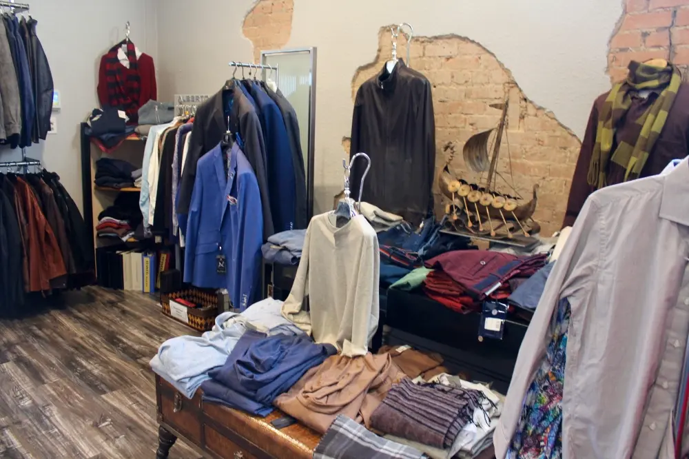 Retail clothing store interior with racks of jackets, coats, and folded garments displayed on wooden tables and mannequins