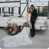Bride and groom posing together beside a vintage white caravan decorated with floral arrangements