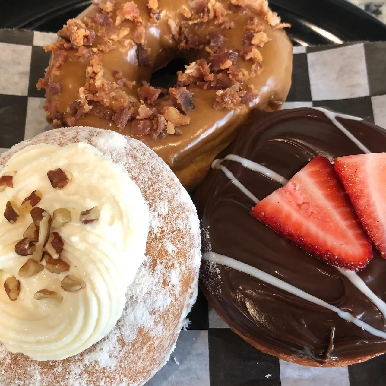 Three donuts: one with caramel glaze and toffee bits, one with cream filling and pistachios, one with chocolate glaze and strawberry slices