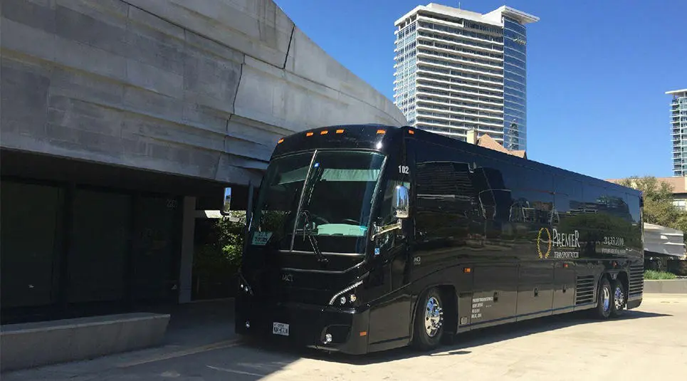 Black motor coach parked beneath concrete overpass with high-rise buildings visible in background