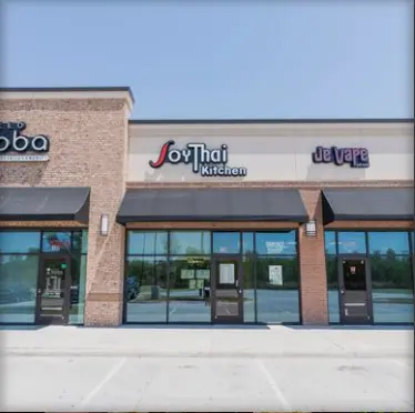 Brick storefront with large windows and glass door entrance, signage reading "JoyThai Kitchen" visible above