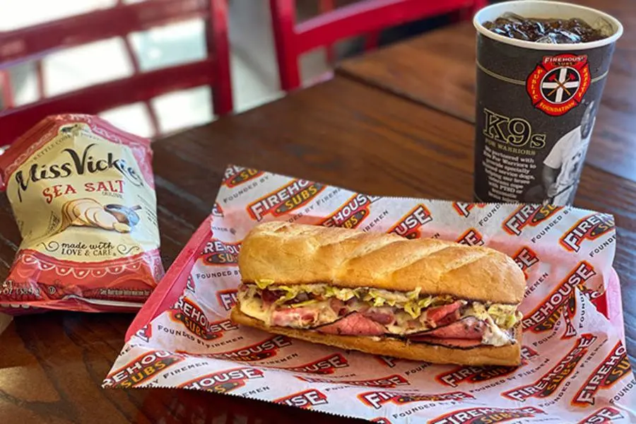 Submarine sandwich with ham, bacon and cheese on toasted roll, served with sea salt chips and cola on wooden table