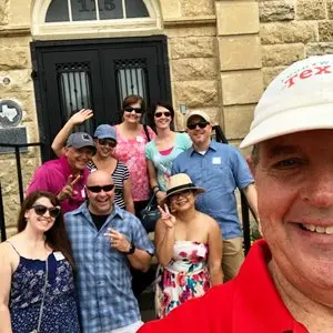 Group of smiling people wearing sunglasses and hats standing together on a historic stone street