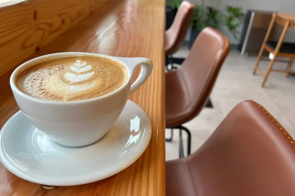 Latte with latte art on wooden table, brown leather chairs visible in cafe seating area