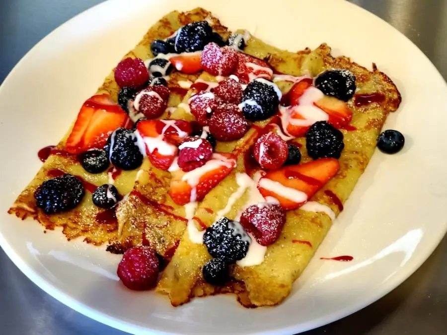 Waffle topped with fresh raspberries, blackberries, strawberries, and whipped cream on a white plate