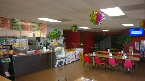 Colorful casual dining interior with counter service area, red accent walls, and pink chairs at dining tables under decorative hanging spheres