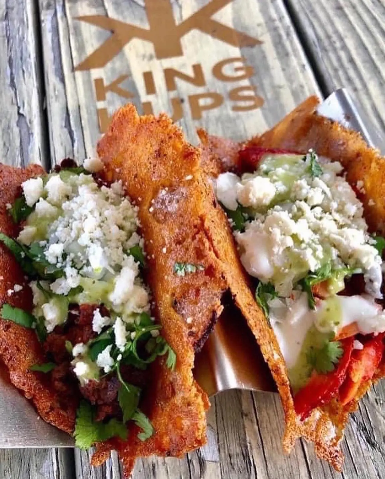 Fried wontons filled with shredded meat topped with crumbled white cheese, diced onion, and cilantro on a wooden surface