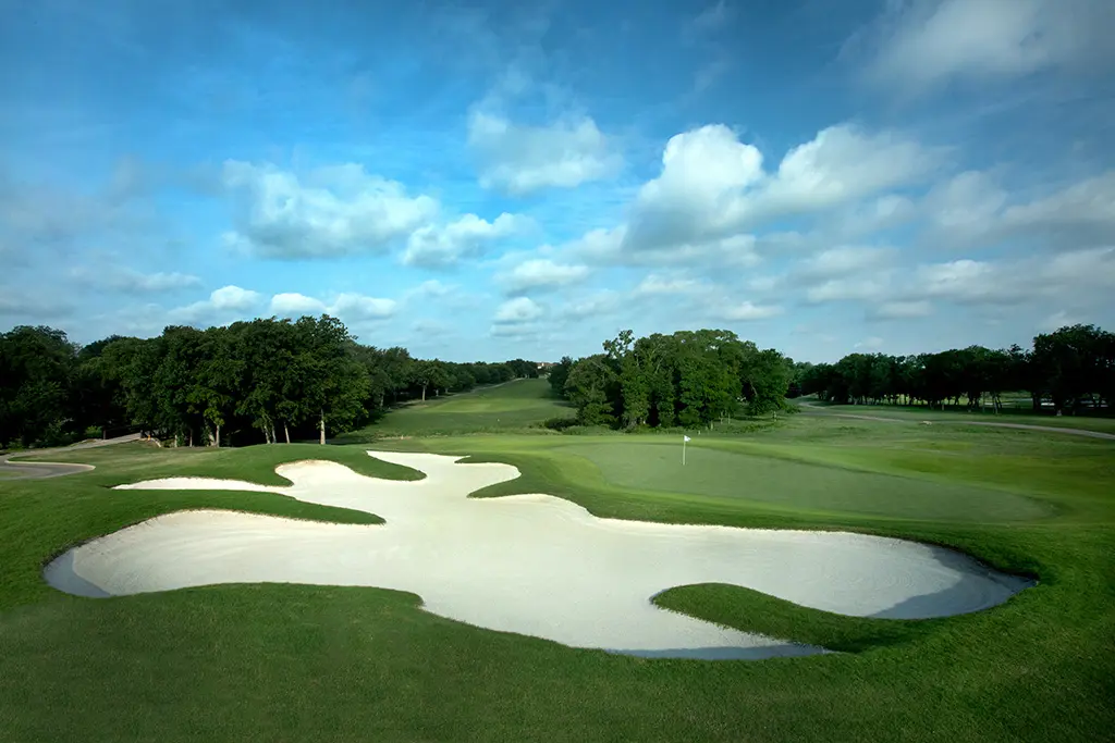 Sand bunker with manicured greens and tree-lined fairways under blue sky